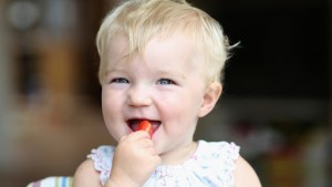 Very happy cute baby girl biting on delicious fresh tomato – es