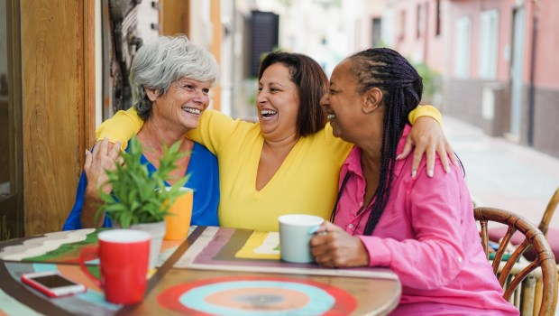Amistad Amigos adultos multirraciales divirtiéndose abrazando en el bar al aire libre mientras toman café juntos