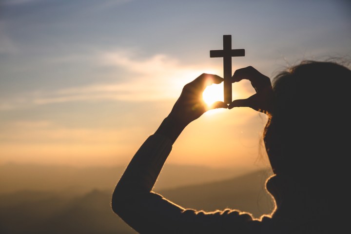 kobieta trzyma w dłoniach krzyż i wznosi go w kierunku słońca