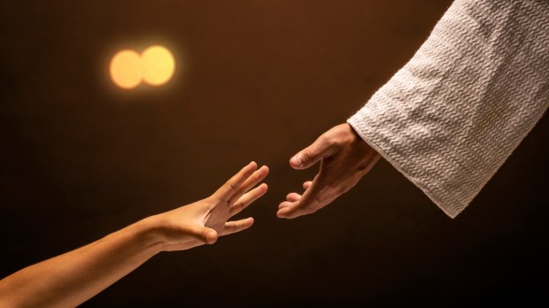 Jesus Christ reaching out to help those in need in a room lit with warm lights