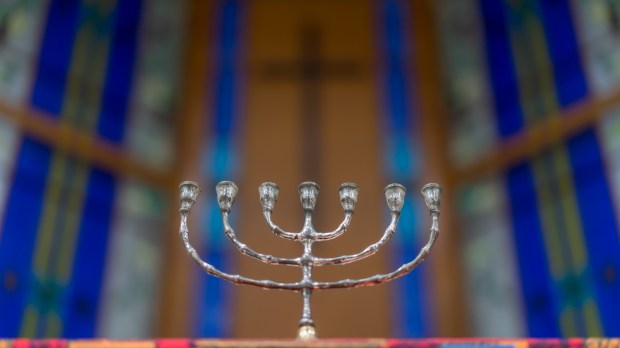 menora stojąca na ołtarzu kościoła z krzyżem na ścianie w tle