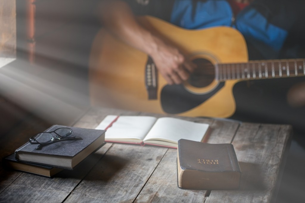 Man plays guitar with bible and open notebook.