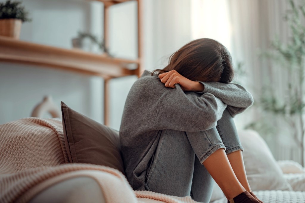 Depressed young woman sitting on couch in the living room at home